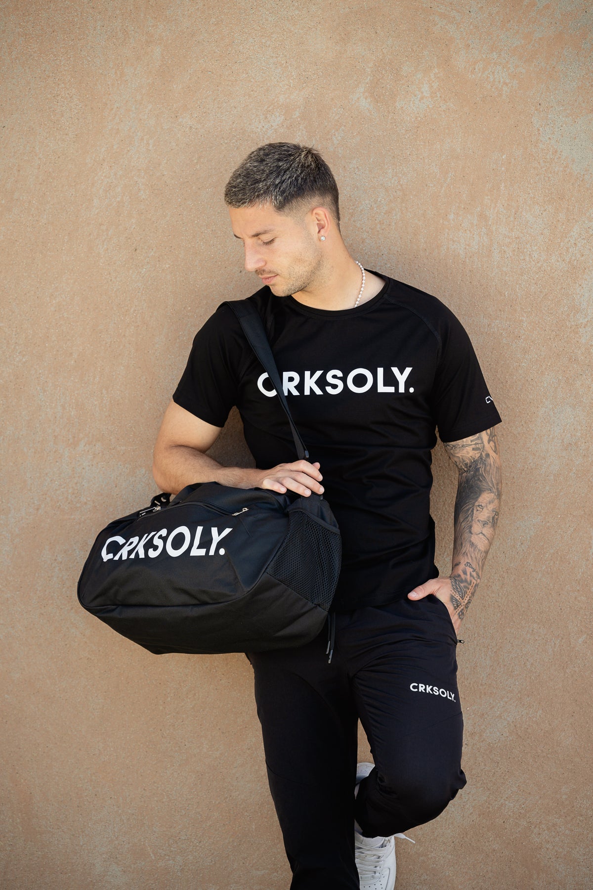 Man in a CRKSOLY. tee carrying a CRKSOLY. duffle bag